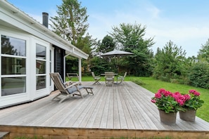 A wooden deck with outdoor furniture, a covered table, and potted plants. - summer cottage with jacuzzi and sauna (Faxe Ladeplads)