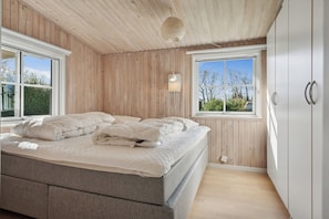 Un dormitorio con cama, paredes de madera, una ventana y un armario.