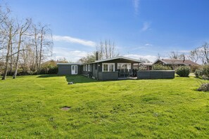 A single-story house with a covered porch, a well-maintained lawn, and a clear sky. - Lovely cottage within walking distance to the sea (Brenderup)