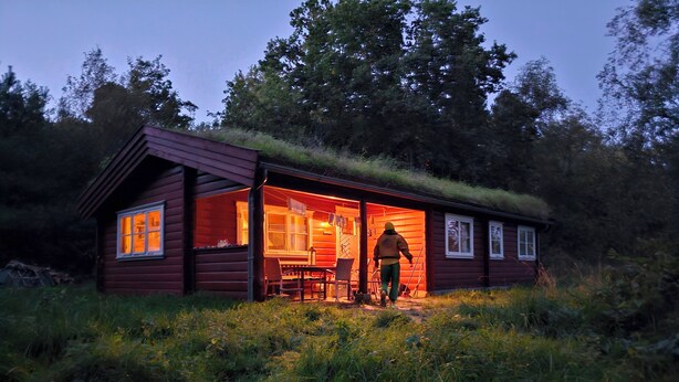 A wooden cabin with a thatched roof, a dining table, and chairs outside. - Charming Norwegian log cabin with grass roof (Ebeltoft)