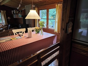 Un comedor con mantel a cuadros, una lámpara colgante, un florero con flores y vistas al exterior.