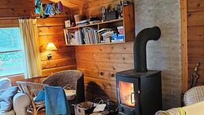 A cozy cabin interior with a wood-burning stove, wicker furniture, and a bookshelf. - Charming Norwegian log cabin with grass roof (Ebeltoft)