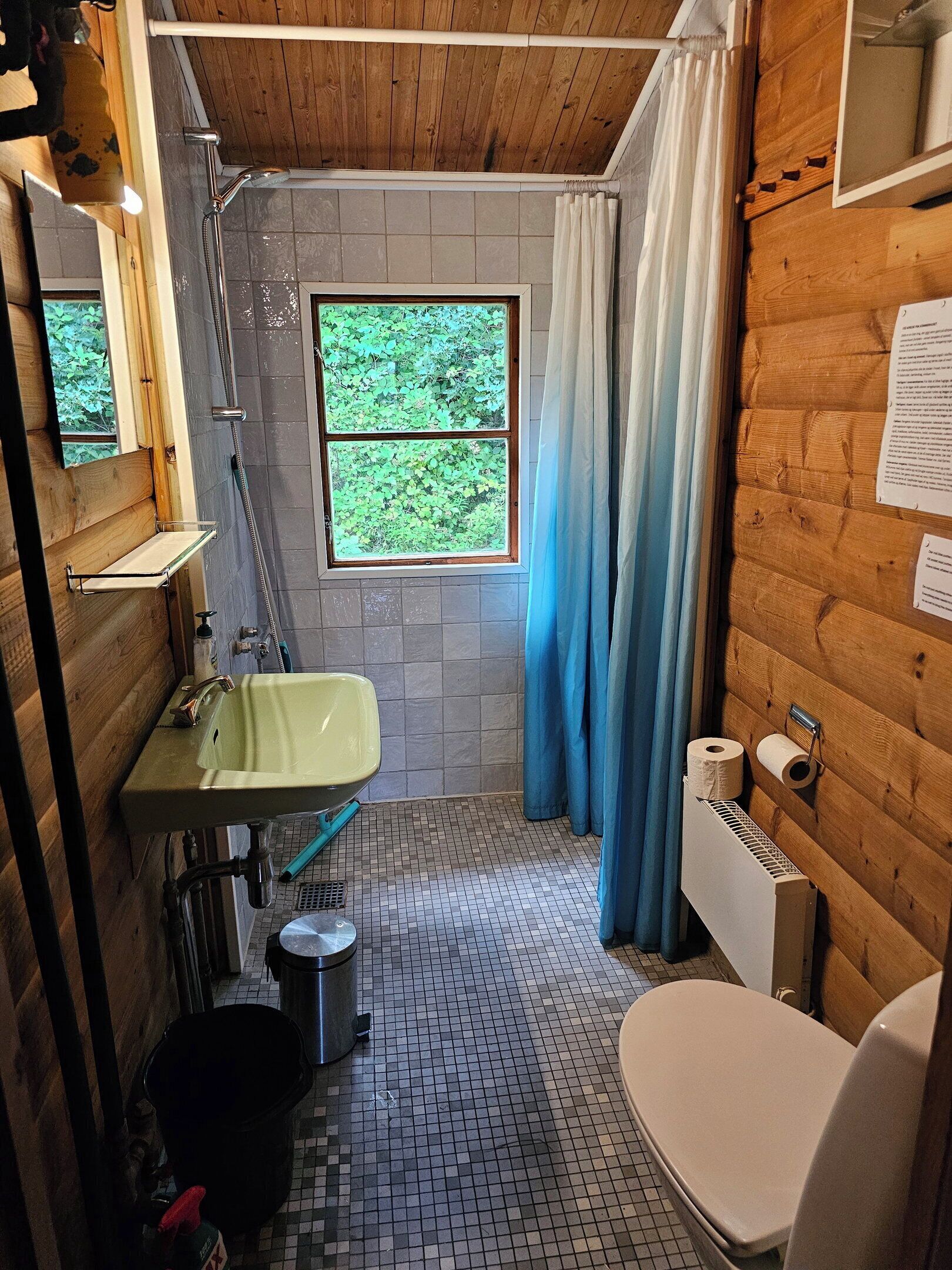 A compact bathroom with a shower, sink, toilet, and a window with a view of greenery.