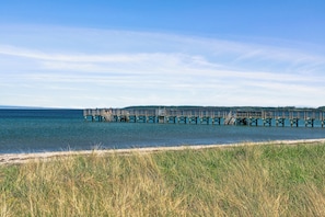 Une jetée s’avançant dans des eaux calmes, entourée de prairies et bordée de collines lointaines.