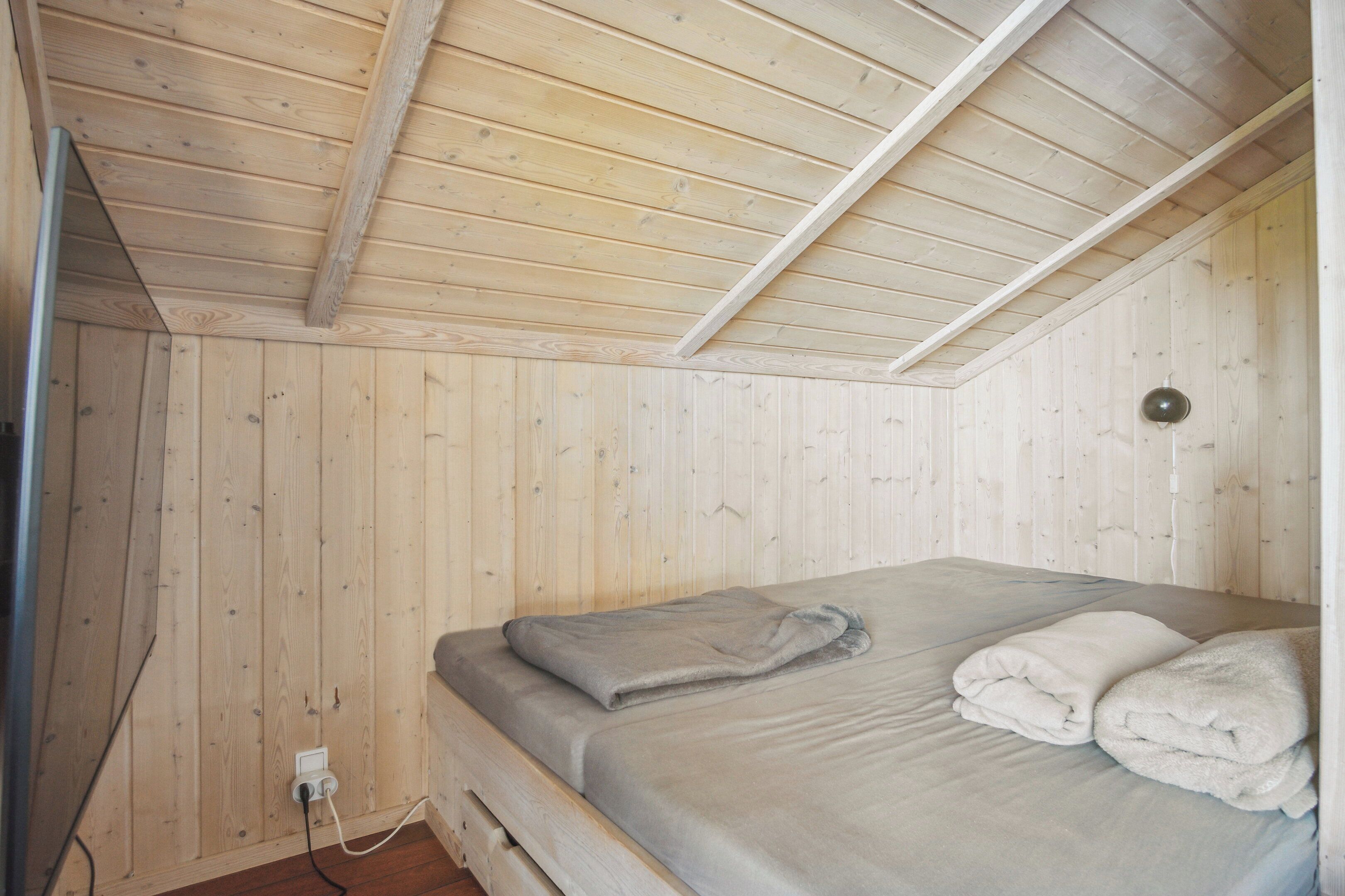 Una habitación con paredes y techo de madera, una cama con colcha gris y un enchufe blanco.