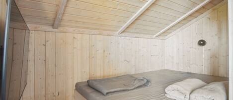 Una habitación con paredes y techo de madera, una cama con colcha gris y un enchufe blanco.