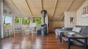 A cozy cabin interior with a wooden ceiling, a fireplace, a sofa, and a dining table. - Beach house with sea view of the Great Belt (Skælskør)