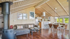 A spacious living area with a fireplace, wooden walls, and a dining area with chairs and a table. - Beach house with sea view of the Great Belt (Skælskør)
