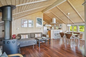 Un vaste espace de vie comprenant un grand poĂȘle Ă bois, un canapĂ©, une table basse et un coin repas avec des chaises.