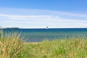 Eine Küstenlandschaft mit einem Leuchtturm in der Ferne, klarem, blauem Wasser und einem grasbewachsen Vordergrund.