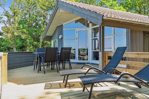 Eine Holzterrasse mit überdachter Sitzecke, einem Tisch und Stühlen.