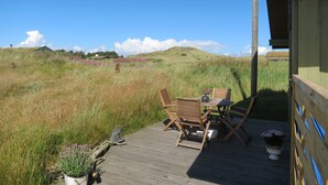 Una terraza de madera con una mesa y sillas, con vistas a un campo verde y una colina al fondo.
