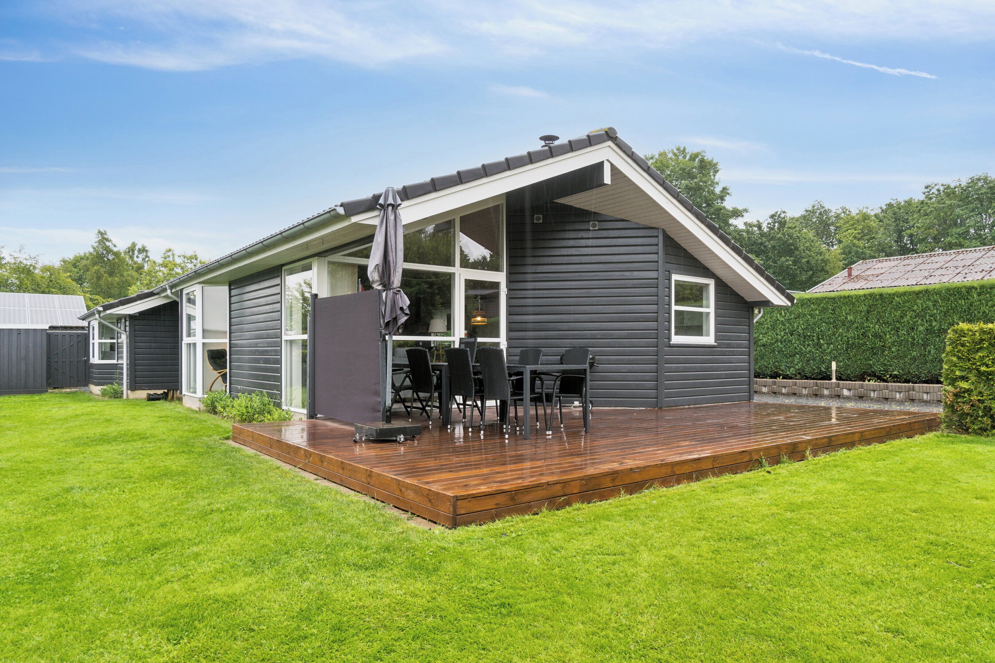 A modern house with a deck, a dining area with chairs and a table, and a large window.