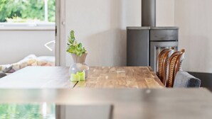 A dining area with a wooden table, chairs, a vase with plants, and a view of greenery outside. - Lovely holiday home Spa/sauna, carcharger, river (Fårvang)