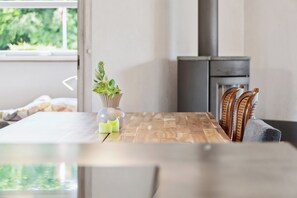 Uma sala de jantar com mesa de madeira, cadeiras, um vaso com plantas e vista para o verde lá fora.