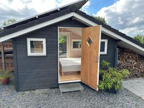 Una cabaña pequeña con puerta de madera, una ventana y una cama en su interior.