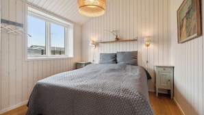 Een slaapkamer met een bed, een raam, een hanglamp, een nachtkastje en een wandlamp.