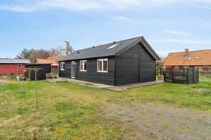 Une maison de plain-pied à l’extérieur sombre, avec un toit en pente et un petit porche à l’avant.