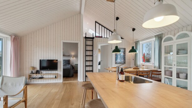 Een ruime keuken met een houten kookeiland, hanglampen en een eethoek met stoelen en een tafel.