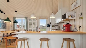 Een keuken met houten aanrechtbladen, barstoelen, hanglampen en uitzicht door het raam.
