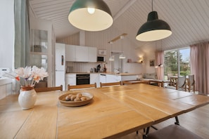 A modern kitchen with wooden cabinets, a dining table, and pendant lighting.