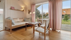 Een gezellige kamer met houten vloer, een bank, een stoel, een tafel en een groot raam met gordijnen.