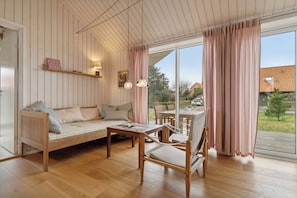 A cozy room with a wooden floor, a sofa, a chair, a table, and a large window with curtains.