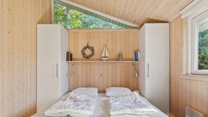 Une chambre à coucher aux murs lambrissés, avec un lit, une étagère ornée d’objets décoratifs et une fenêtre.