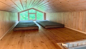 Ein Zimmer mit Holzwänden, einer schrägen Decke, zwei Betten und einem großen Fenster.