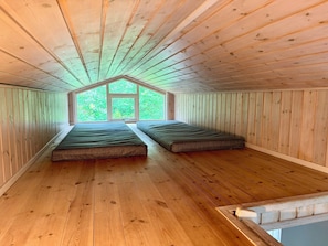 Une pièce aux murs en bois et au plafond en pente, avec deux lits et une grande fenêtre.