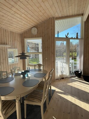 A wooden-paneled room with a dining table, chairs, a clock, and large windows. - Charming house in the heart of WestZealand (Eskebjerg)