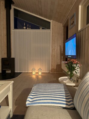 A cozy room with a wooden interior, a television mounted on the wall, a small table with a vase of flowers, and a sofa with striped cushions. - Charming house in the heart of WestZealand (Eskebjerg)