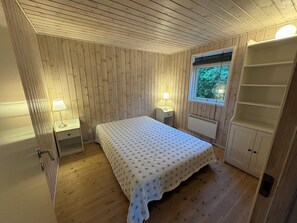 Et rum med træpaneler, en seng, to sengeborde med lamper, et vindue og en indbygget reol.
