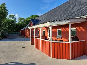 A red building with a porch, a metal roof, and a gravel driveway.
