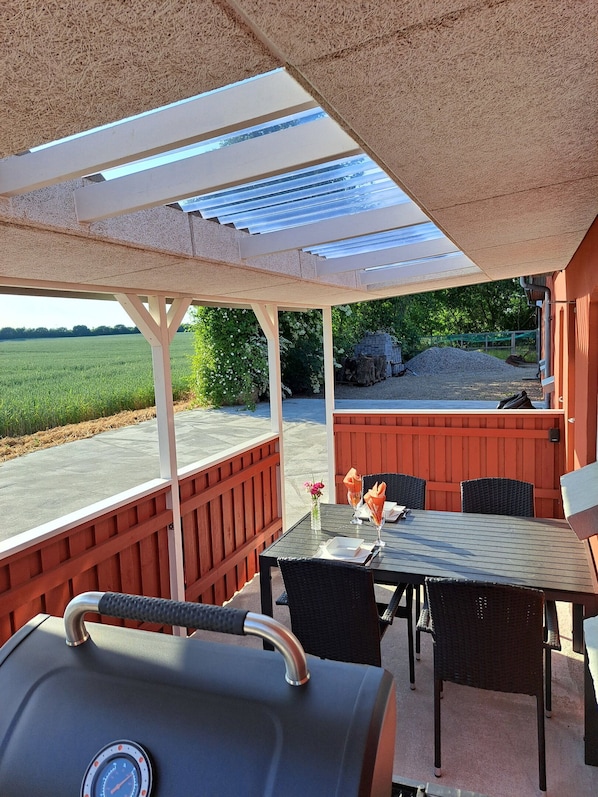 An outdoor patio with a grill, dining table, chairs, and a view of a field.
