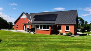 A house with a solar panel on the roof, a red exterior, and a well-maintained lawn.