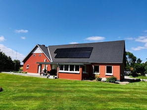 A house with a solar panel on the roof, a red exterior, and a well-maintained lawn.