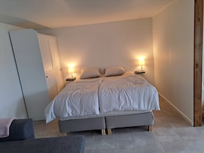 A bedroom with a bed, bedside lamps, a wardrobe, and a chair. - Idyllic country apartment incl all utilities (Christiansfeld)