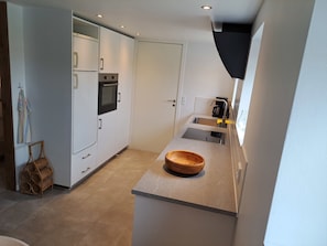 A compact kitchen with white cabinets, a built-in oven, a sink, and a wooden bowl on the countertop. - Idyllic country apartment incl all utilities (Christiansfeld)