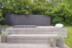 A wooden deck with a hot tub, steps, and wicker planters.