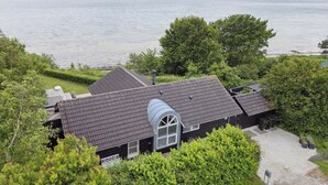 Een huis met een schuin dak, een groot rondboogvenster en uitzicht op een wateroppervlak.