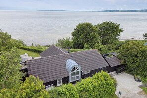 Ein Haus mit einem geneigten Dach, einem großen Rundbogenfenster und Blick auf ein Gewässer.