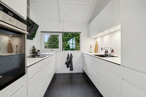 Eine moderne Küche mit weißen Schränken, einem eingebauten Backofen, einem Fenster und einem Haken für Handtücher.
