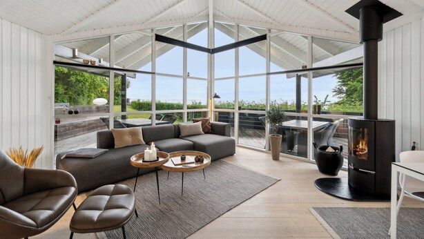 Een moderne woonkamer met een hoekbank, een open haard en grote ramen met uitzicht op de natuur.