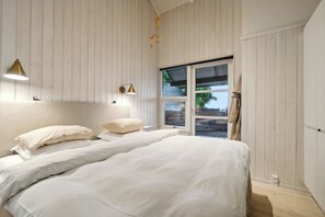 A bedroom with two beds, a window, and a wall-mounted light fixture.