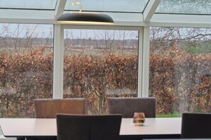 A dining area with a table and chairs, a glass ceiling, and a view of a leaf-covered landscape.