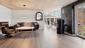 A modern interior with a wooden ceiling, a black leather sofa, a dining table, and a fireplace.