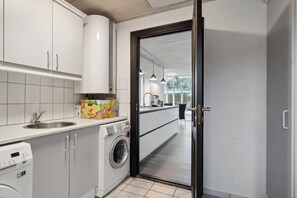 A modern kitchen with a washing machine, a sink, and a dining area visible through an open door.