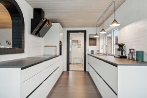 A modern kitchen with white cabinetry, a wooden floor, and pendant lighting.