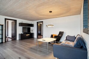 A modern living room with a wooden ceiling, a sofa, a coffee table, and a TV.